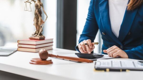 Lawyer calculating expenses, with a legal contract, gavel, and law books on the table.